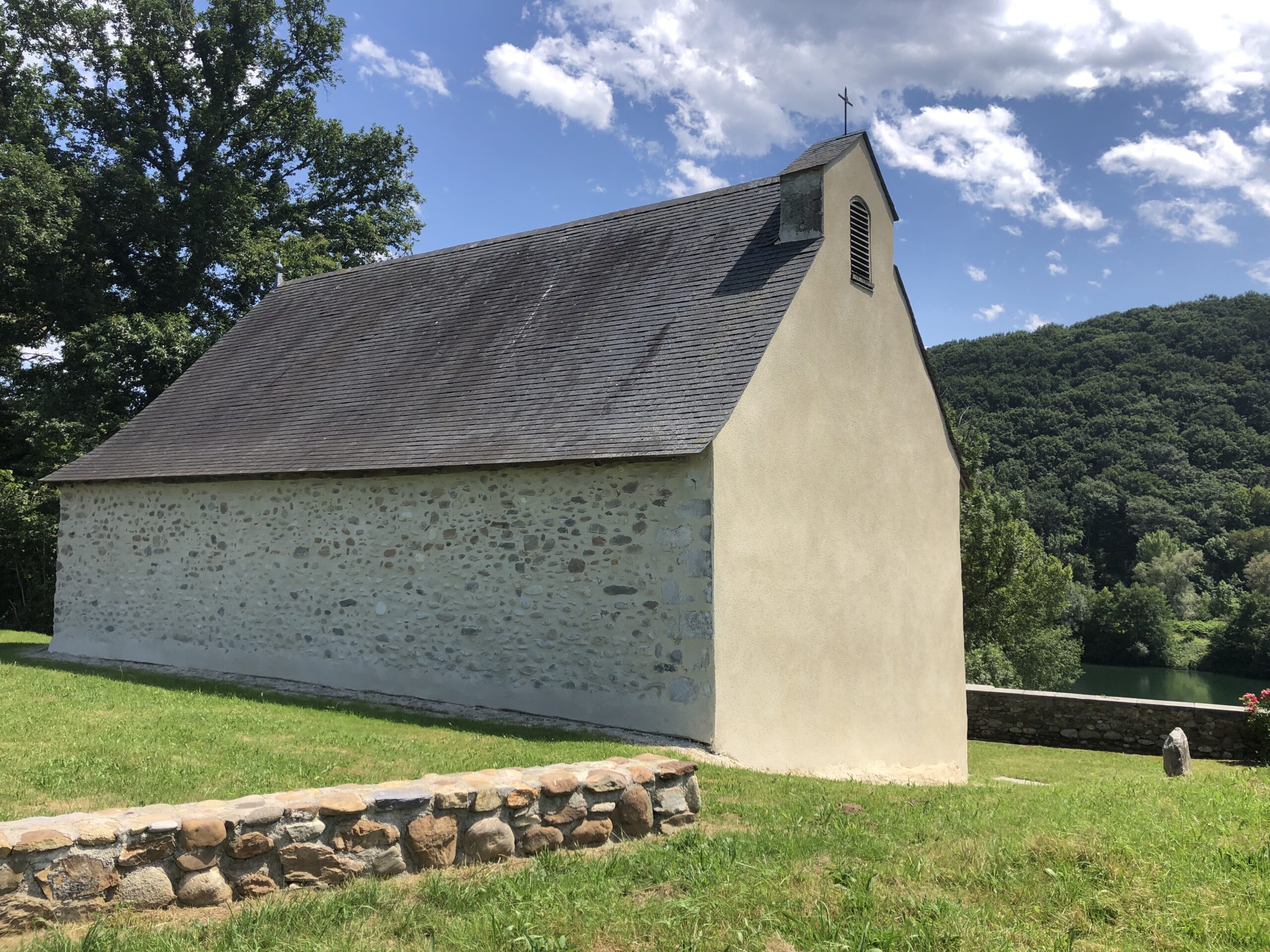 Chapelle de Mour vue de l'extérieur. On la voit bien implantée dans un écrin de verdure. Sa façade est en partie en pierre apparente.